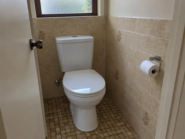 Small tiled toilet room with a white toilet and paper holder in Eastgardens