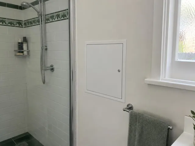 Bathroom wall with a small access panel beside a shower and towel rail in Kensington